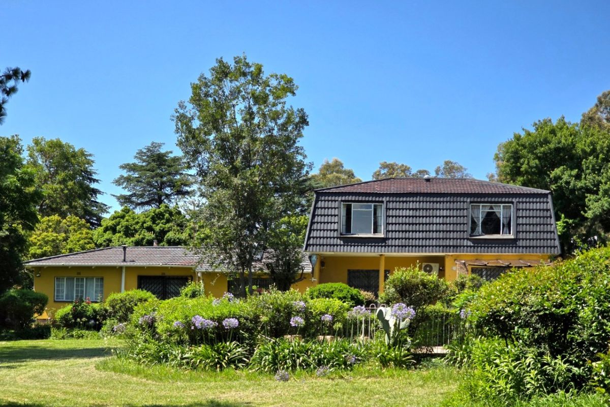 A view of the rear elevation of a two-story house featuring a mansard roof, yellow exterior walls, and established garden landscaping.
