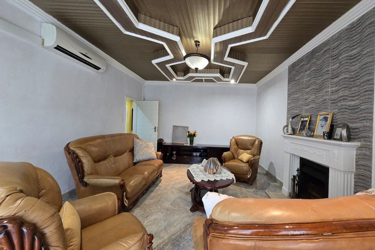 A living room featuring a distinctive decorative coffered ceiling, a fireplace with a mantelpiece, and tiled flooring.