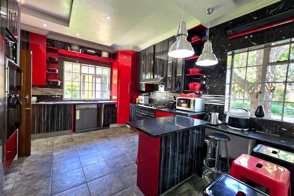 A modern kitchen featuring high-gloss red and dark wood cabinetry, stone countertops, integrated appliances, and large windows providing ample natural light.