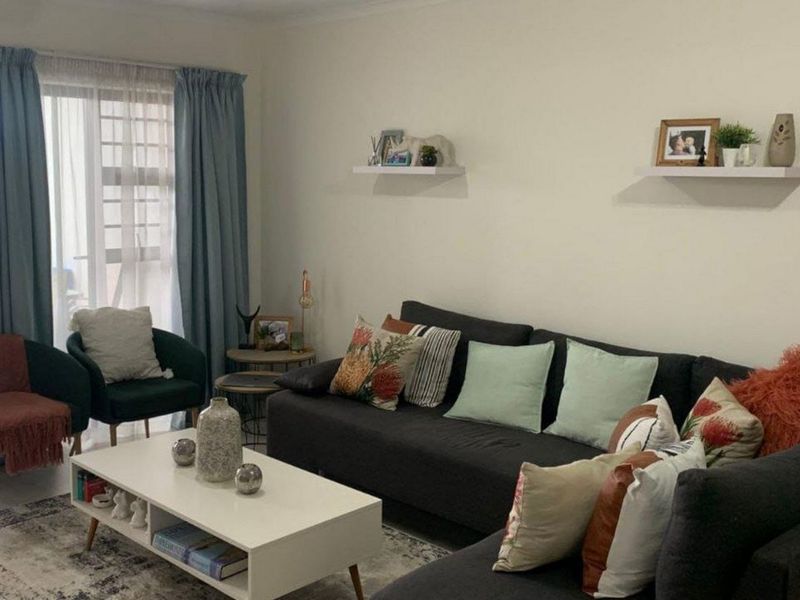A well-maintained living room featuring tiled flooring, neutral walls, and a large sliding glass door providing access to an outdoor area.