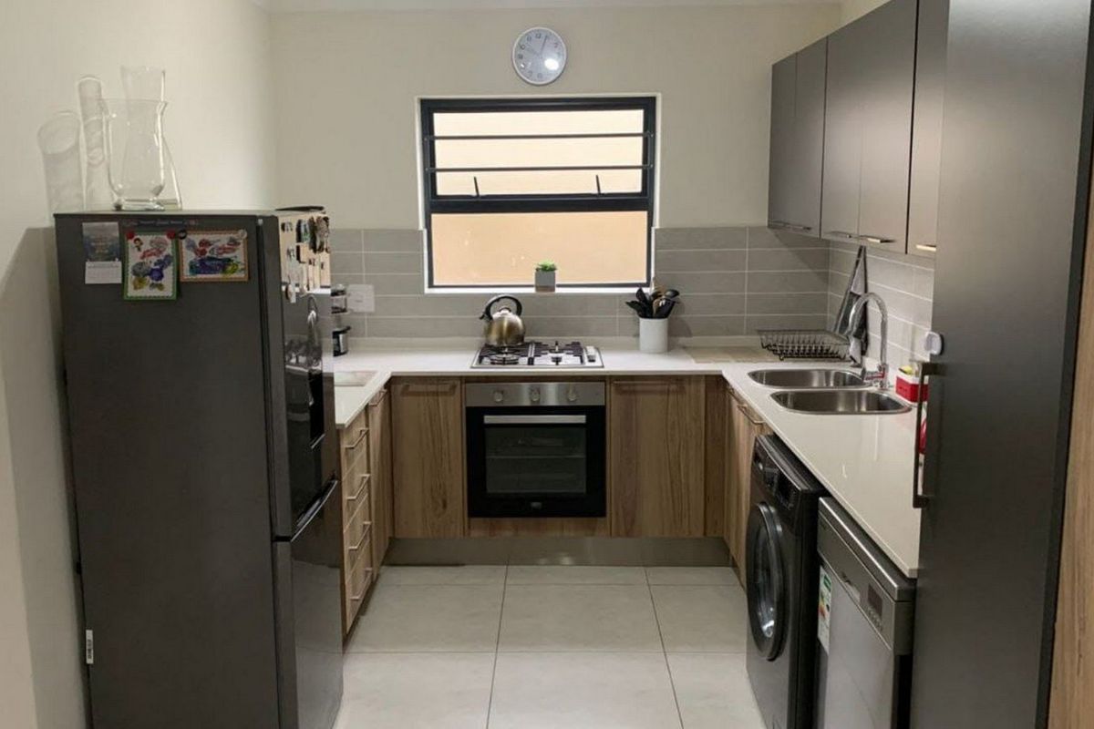 Modern U-shaped kitchen featuring wood-grain lower cabinetry, grey upper cabinets, stone countertops, built-in oven, gas hob, and integrated laundry plumbing.