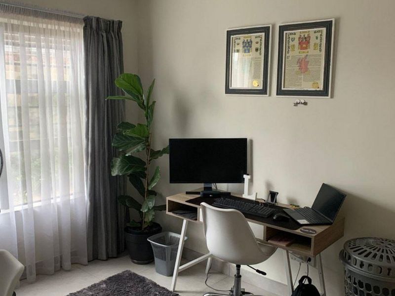 A functional home office space featuring neutral wall finishes, tiled flooring, and a large window with curtain treatments.
