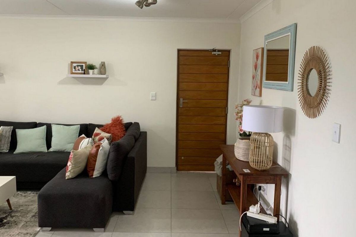 A well-maintained living room featuring neutral tiled flooring and a solid timber entrance door.