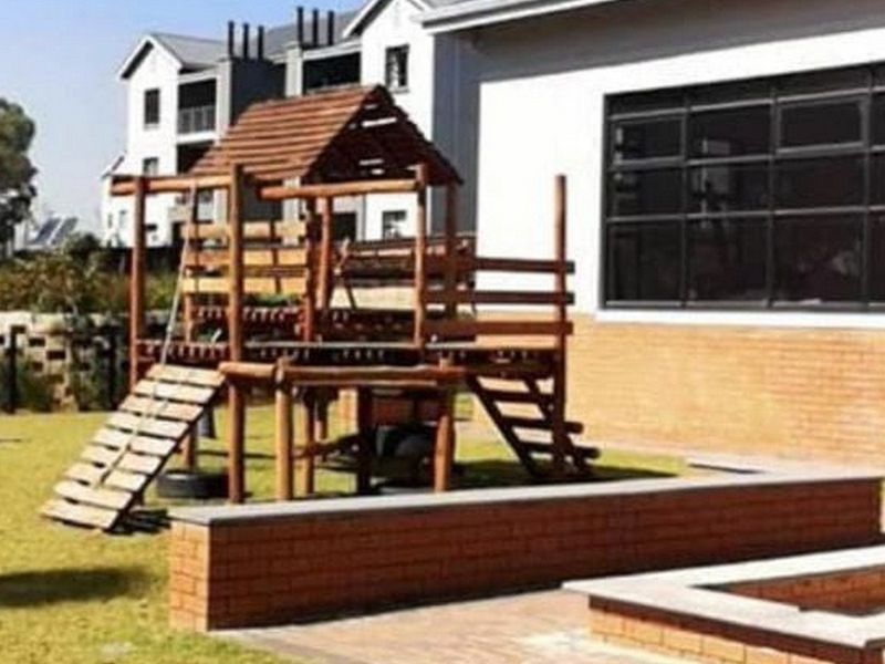 A communal garden area featuring a brick retaining wall, paved sections, and a large window overlooking the outdoor space.