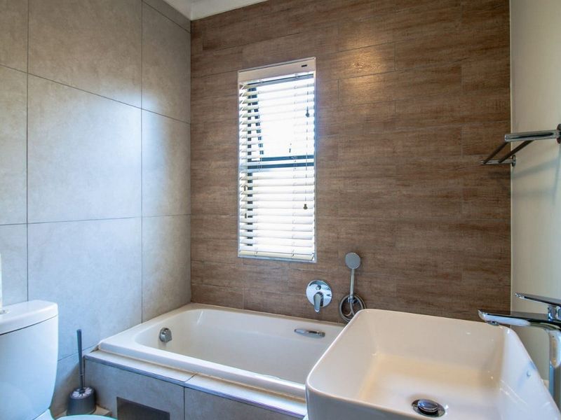 Modern bathroom featuring a built-in bathtub, vessel sink with chrome fixtures, and stylish wood-look and neutral ceramic wall tiling.
