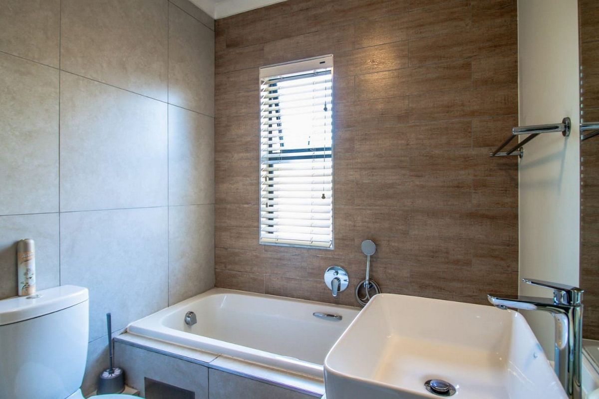 Modern bathroom featuring a built-in bathtub, vessel sink with chrome fixtures, and stylish wood-look and neutral ceramic wall tiling.