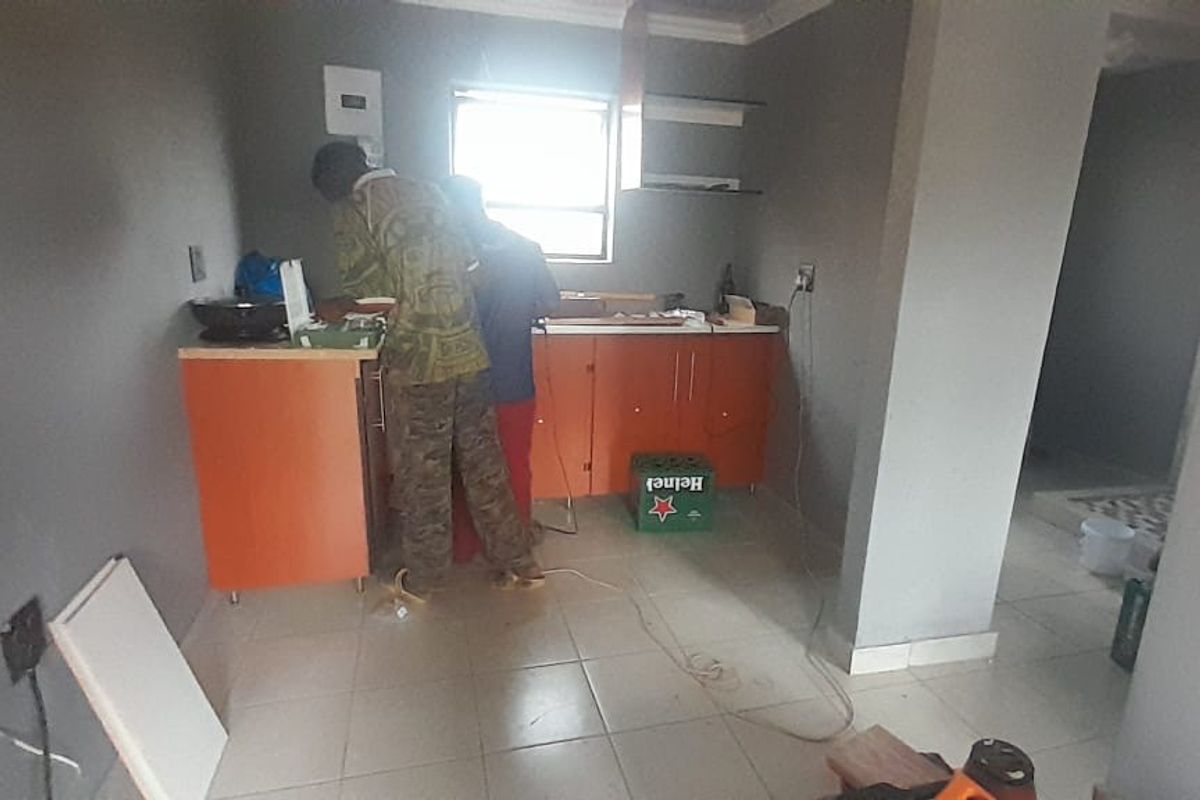 A kitchen area currently undergoing renovation with installed base cabinetry, tiled flooring, and visible electrical work in progress.