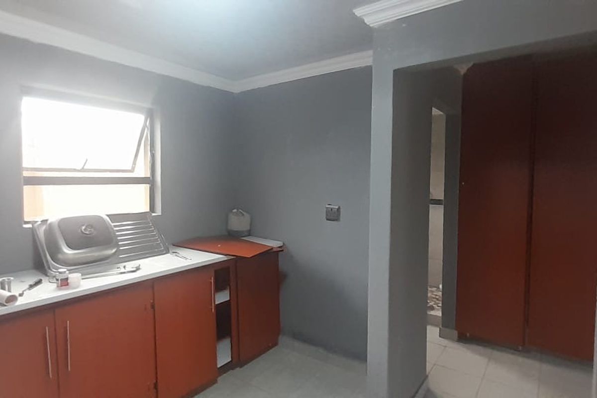 A functional kitchen space featuring built-in cabinetry, a stainless steel sink, and tiled flooring, currently in a state of partial completion.