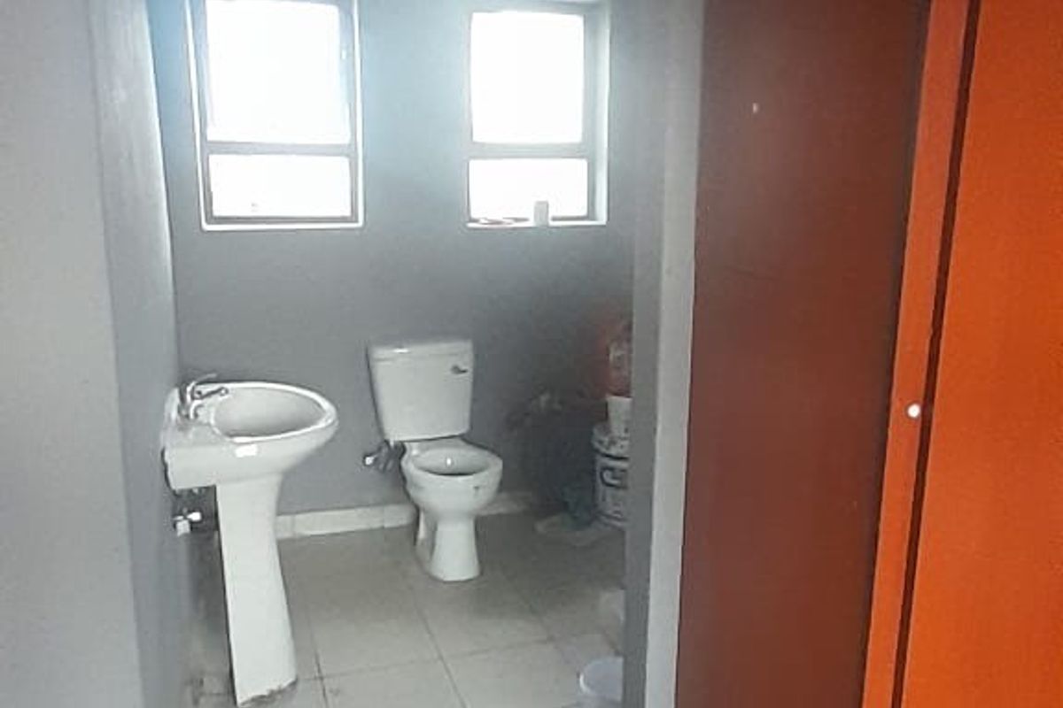 A functional bathroom featuring a pedestal basin, toilet, and tiled flooring, requiring cosmetic updates to improve its overall condition and appeal.