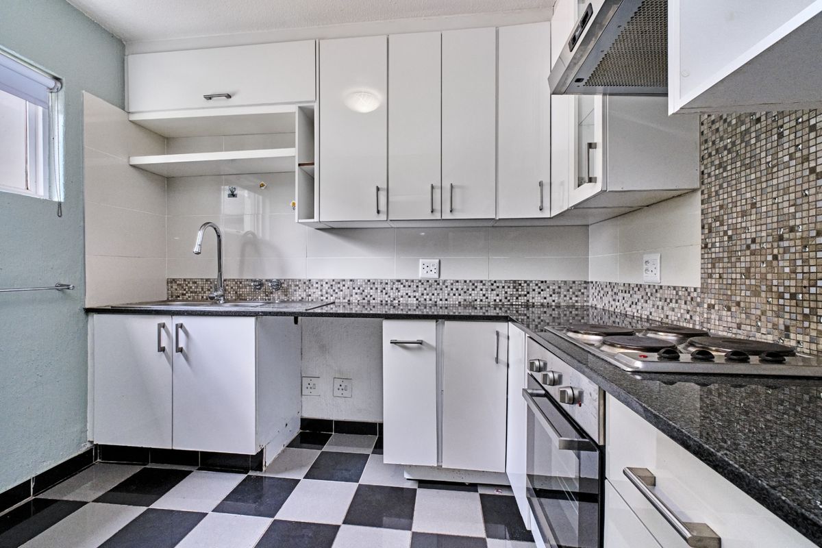 Functional kitchen featuring white cabinetry, granite countertops, mosaic tile backsplash, built-in oven, hob, and extractor fan with checkered floor tiles.