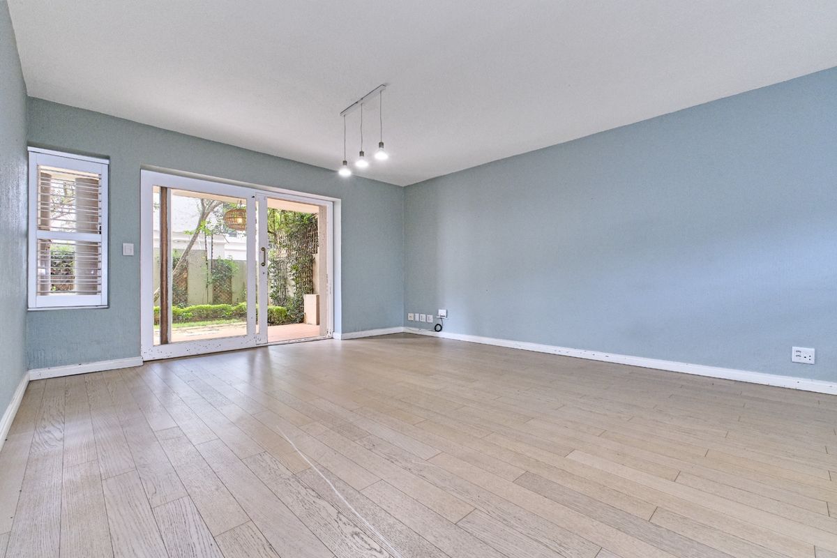A bright, empty living room featuring light-toned wood flooring, blue-painted walls, and sliding glass doors that open onto a private patio area.