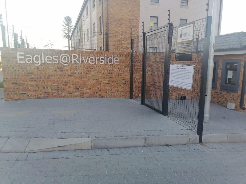 The entrance to Eagles@Riverside apartment complex featuring a brick boundary wall, security gate, and electric fencing.