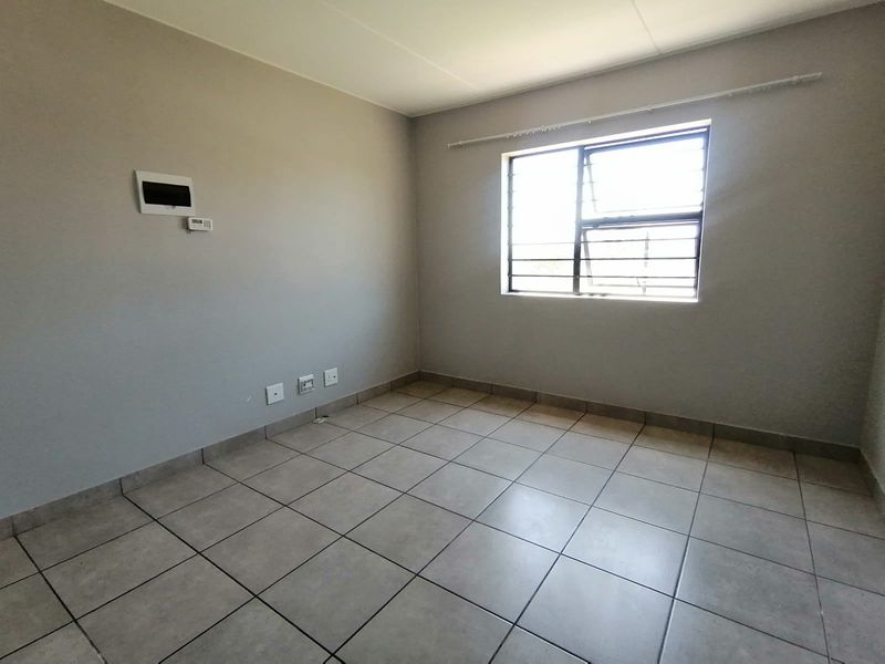 A clean, empty bedroom featuring neutral wall paint, tiled flooring, and a window fitted with security bars.