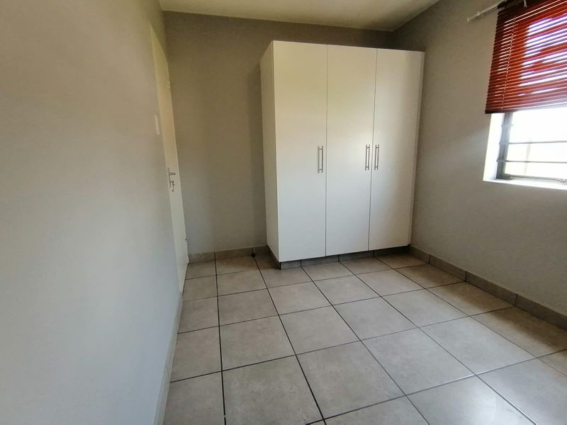 A clean, empty bedroom featuring neutral tiled flooring, a built-in wardrobe, and a window fitted with venetian blinds.