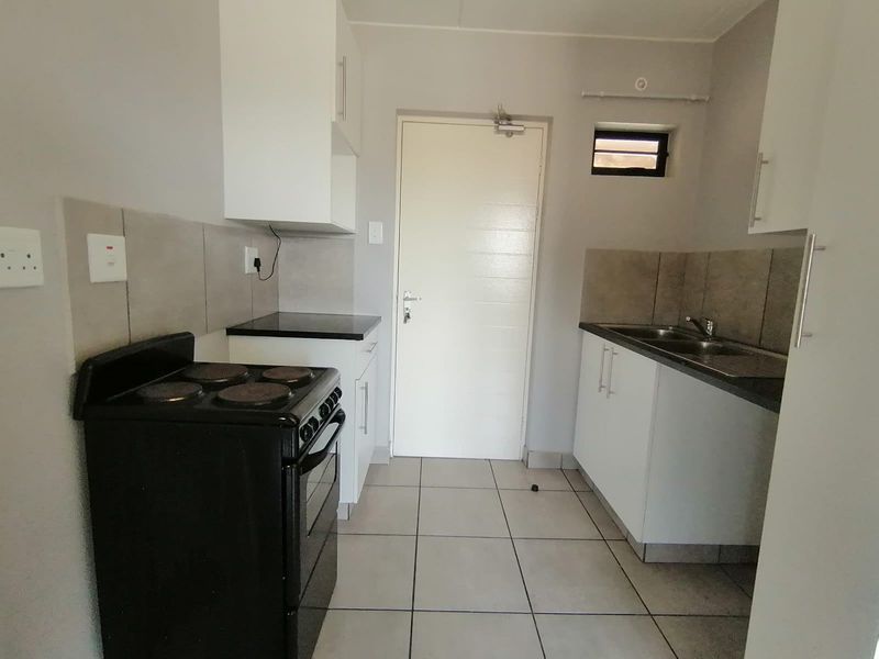 A functional kitchen featuring white cabinetry, tiled backsplash, double sink, and tiled flooring, providing a clean and practical workspace.