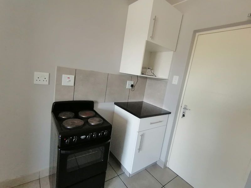 A compact kitchen area featuring white built-in cabinetry, a black granite countertop, tiled backsplash, and a freestanding electric stove.