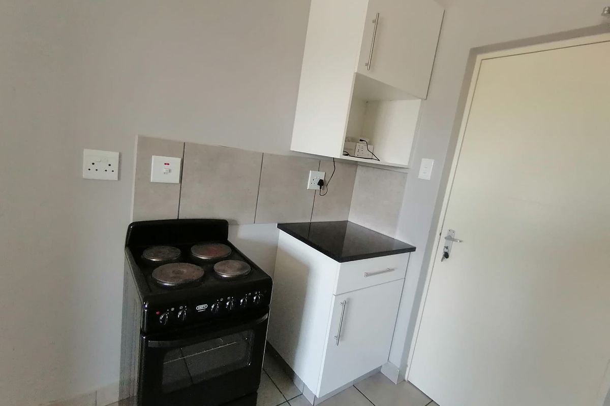 A compact kitchen area featuring white built-in cabinetry, a black granite countertop, tiled backsplash, and a freestanding electric stove.