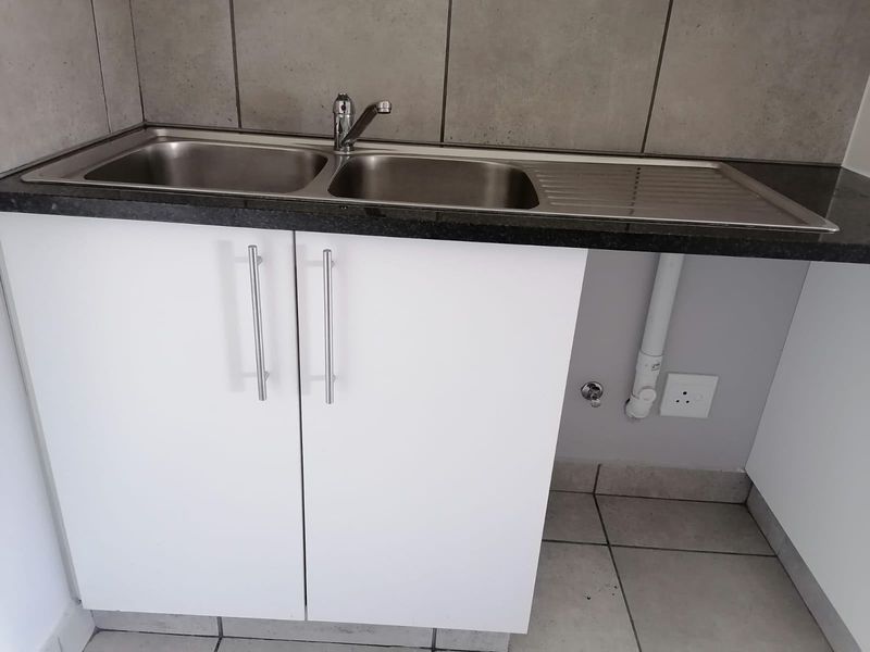 A clean kitchen area featuring a stainless steel double sink, granite countertop, and white cabinetry with tiled splashback and flooring.