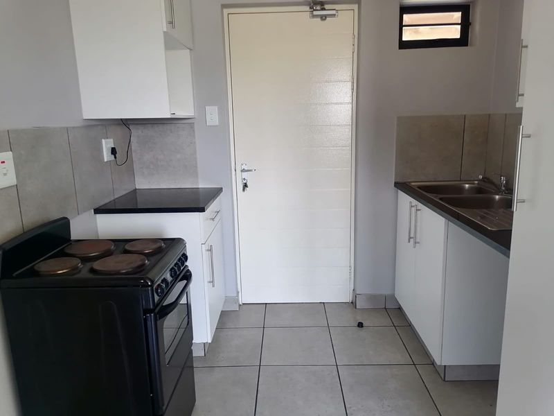 A functional kitchen featuring white cabinetry, dark countertops, tiled splashbacks, and a double sink, providing a clean and practical workspace.