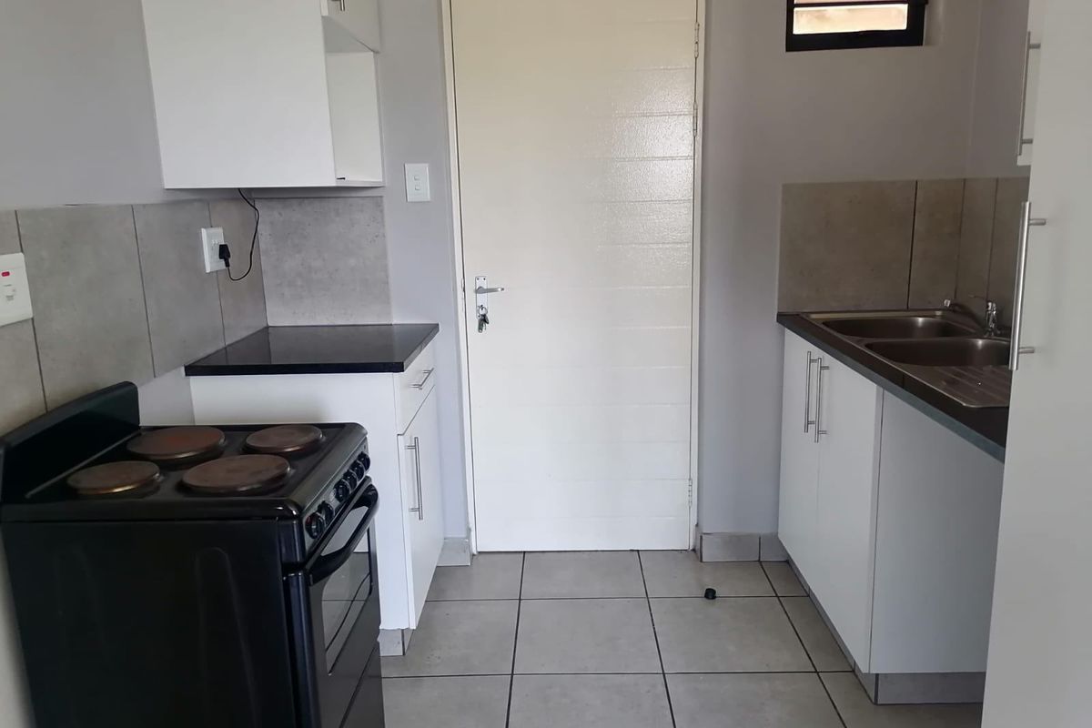 A functional kitchen featuring white cabinetry, dark countertops, tiled splashbacks, and a double sink, providing a clean and practical workspace.