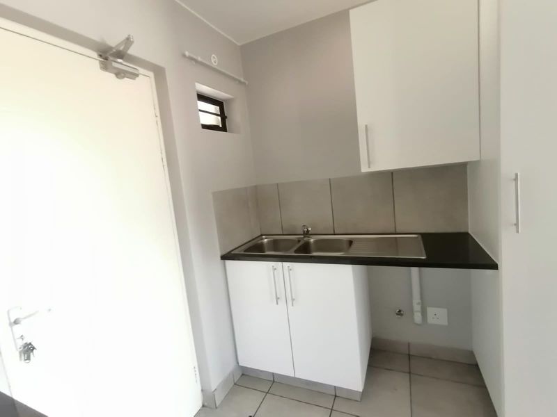 A compact kitchen area featuring built-in white cabinetry, a stainless steel double sink, tiled splashback, and tiled flooring.