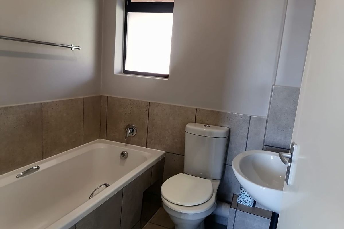 A functional bathroom featuring a bathtub, pedestal basin, and toilet with neutral wall tiling and a window for natural light.