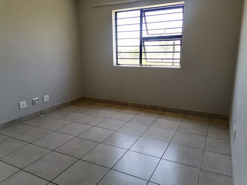 An empty bedroom featuring neutral tiled flooring, plain walls, and a window fitted with security bars.