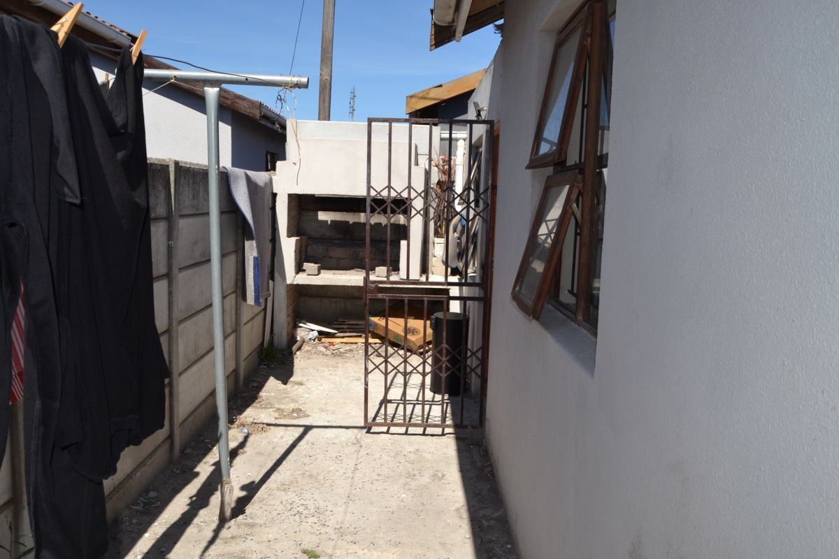 Rear exterior area featuring a built-in braai, concrete boundary wall, and security gate access, requiring maintenance and cosmetic updates.