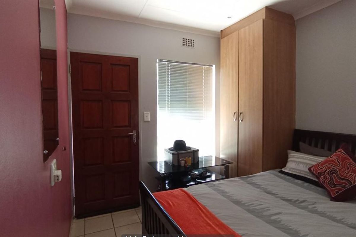 A bedroom featuring built-in wooden wardrobes, tiled flooring, and a solid timber door with access to natural light through a window with blinds.