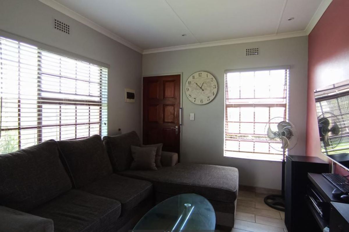 A comfortable living room featuring tiled flooring, large windows with venetian blinds, and a feature wall, providing a functional and well-lit space.