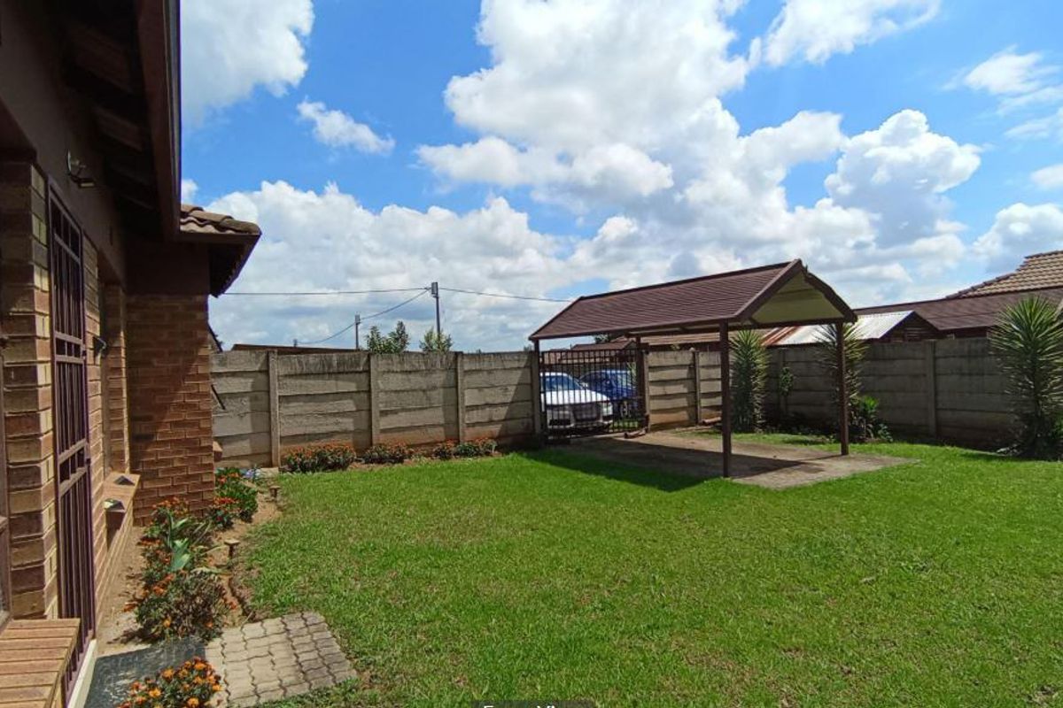 Rear garden area featuring a lawn, paved driveway, and a covered carport structure enclosed by a precast concrete boundary wall.