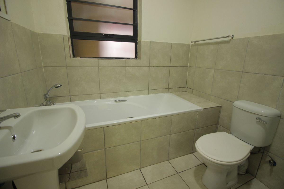 A functional bathroom featuring a pedestal basin, built-in bathtub, and toilet with neutral wall and floor tiling.
