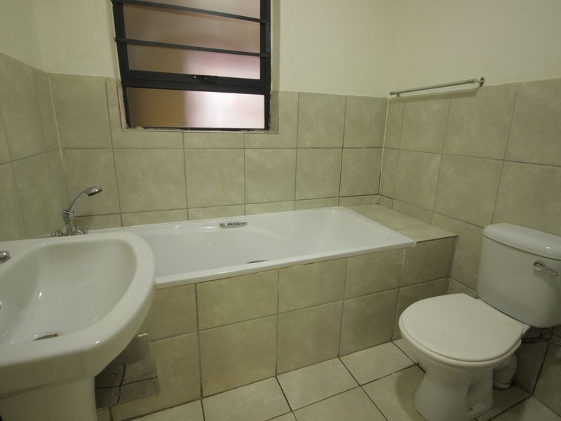 A functional bathroom featuring a pedestal basin, built-in bathtub, and toilet with neutral wall and floor tiling.