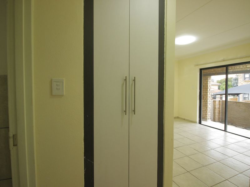 A bright hallway featuring a built-in cupboard, leading into an open-plan living area with tiled floors and access to an outdoor patio.