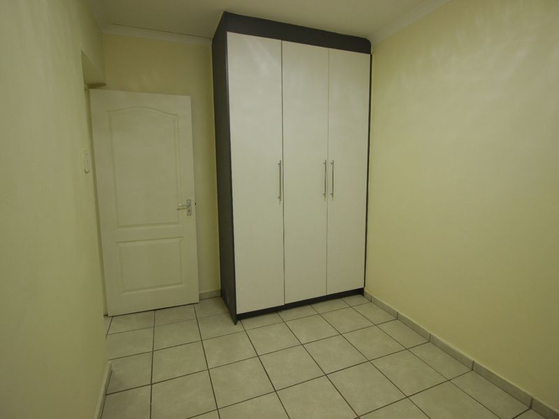 A clean, empty bedroom featuring neutral tiled flooring and a modern built-in wardrobe with white doors and dark framing.
