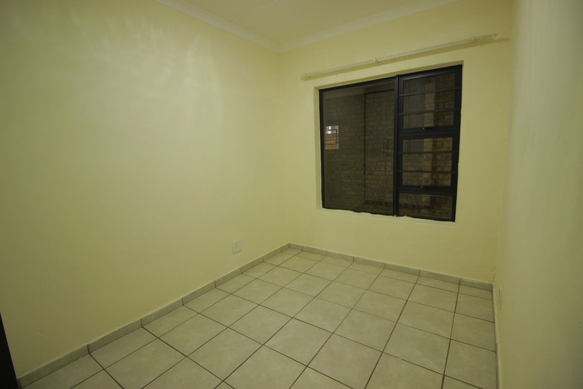 A clean, empty bedroom featuring neutral walls, tiled flooring, and an aluminium-framed window with security bars.