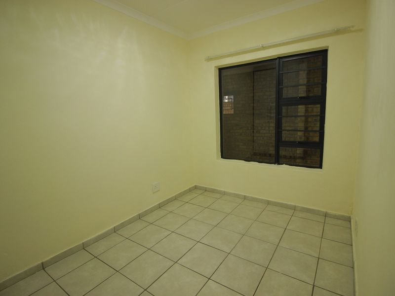 A clean, empty bedroom featuring neutral walls, tiled flooring, and an aluminium-framed window with security bars.