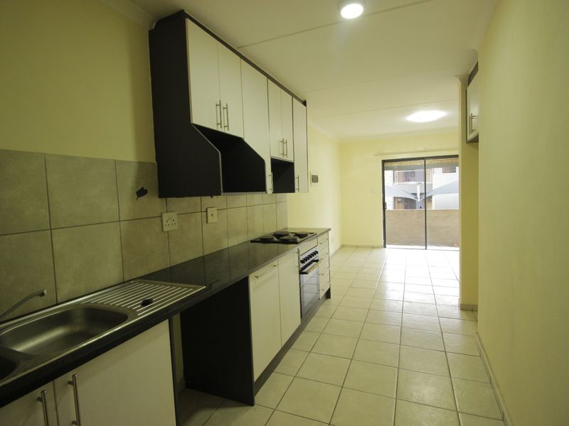 An empty kitchen featuring built-in cabinetry, granite countertops, a built-in oven, and tiled flooring, leading to a sliding glass door.