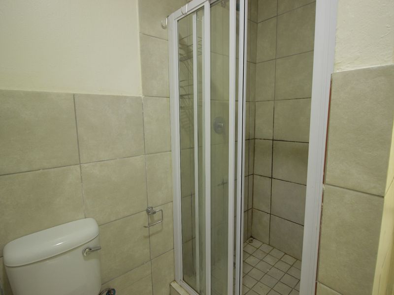 A functional bathroom featuring a shower enclosure and toilet with neutral wall and floor tiling, requiring some maintenance to the grout and fixtures.