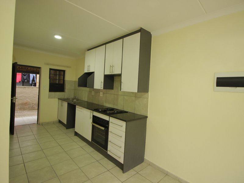 A clean, functional kitchen featuring modern two-tone cabinetry, granite countertops, a built-in oven with hob, and tiled flooring with direct access to an outdoor area.