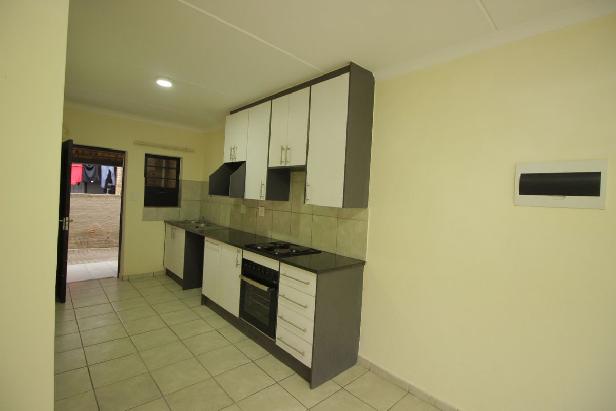 A clean, functional kitchen featuring modern two-tone cabinetry, granite countertops, a built-in oven with hob, and tiled flooring with direct access to an outdoor area.