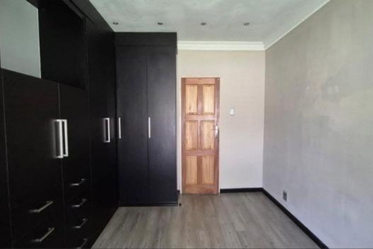 A bedroom featuring dark built-in cupboards, laminate flooring, and recessed ceiling lighting, providing a clean and functional space ready for personalization.