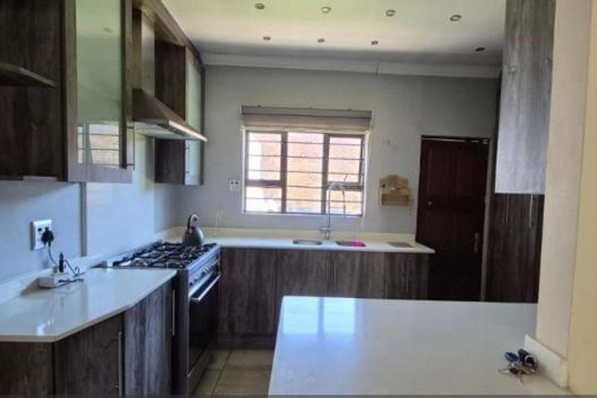 A modern kitchen featuring dark wood cabinetry, stone countertops, a gas hob with extractor fan, and a double sink with a window view.