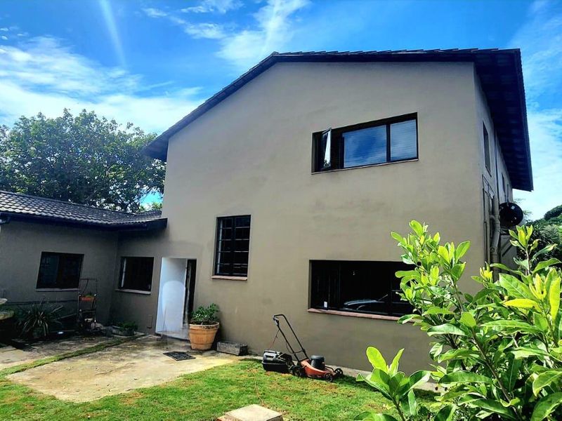 Rear view of the two-story house featuring a concrete patio, landscaped garden area, and tiled roof structure.