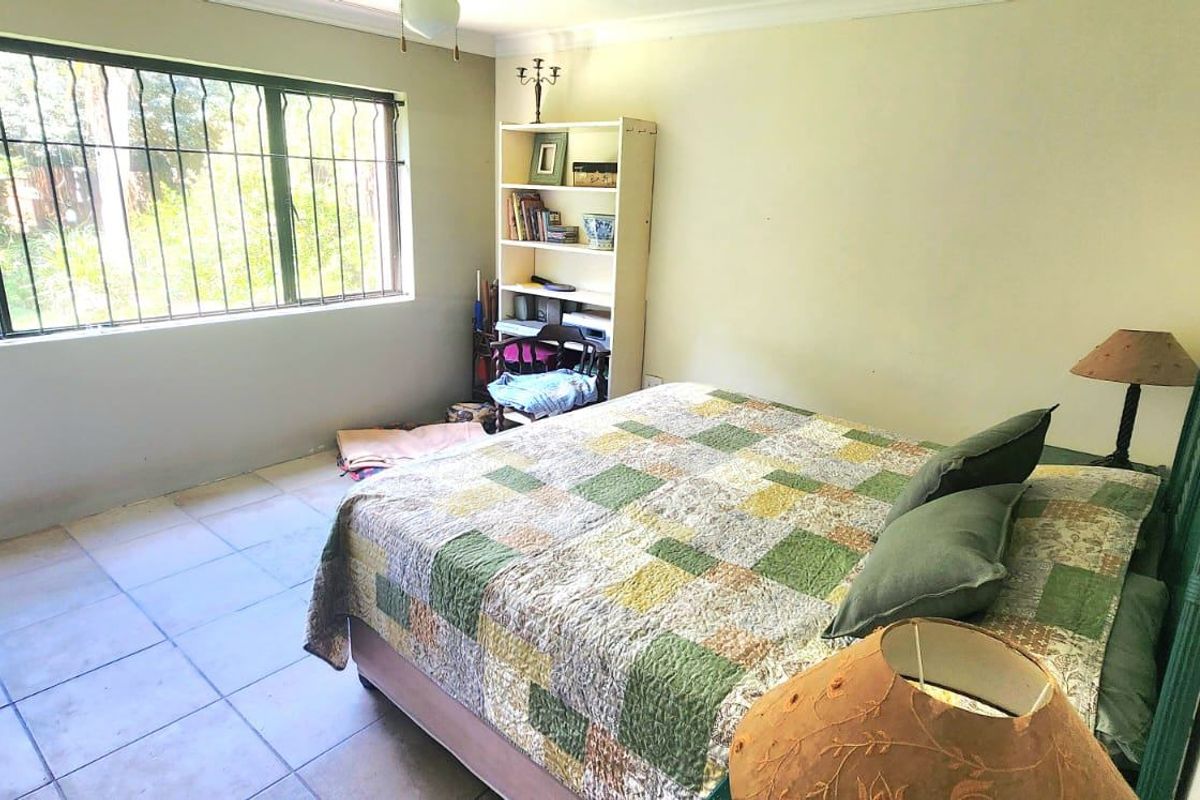 A bedroom featuring tiled flooring, a ceiling fan, and large windows fitted with security bars, offering a functional and well-lit living space.
