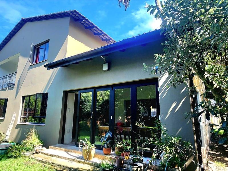 Rear view of a two-story house featuring a tiled roof, aluminium windows, sliding glass doors leading to a patio, and an upper-level balcony.