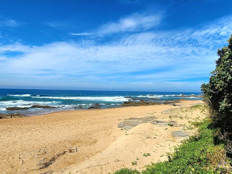 A scenic view of the sandy beach, rocky coastline, and ocean waves under a clear blue sky.