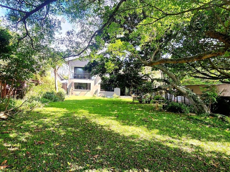 A spacious rear garden featuring a lush lawn, mature trees, and a timber boundary fence, providing a private outdoor setting for the property.
