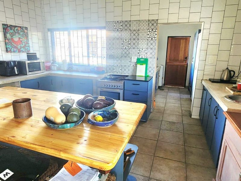 A functional kitchen featuring blue cabinetry, tiled splashbacks, a central wooden island, and tiled flooring with direct access to an adjacent utility area.
