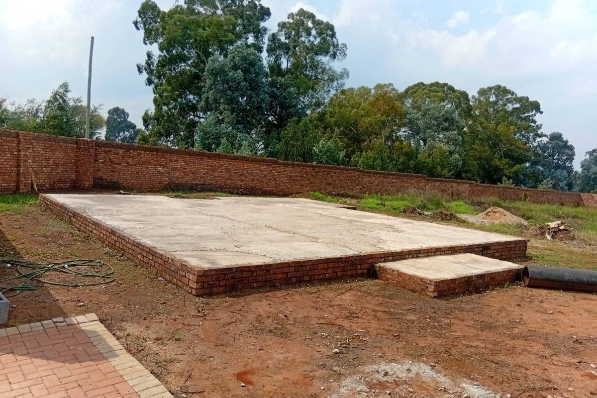 An outdoor area featuring a concrete slab foundation and brick boundary wall, currently in an unfinished state.